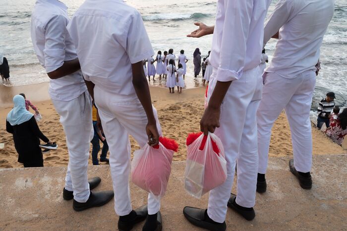 Group of young men dressed in white holding bags near the beach, capturing street photography moments.