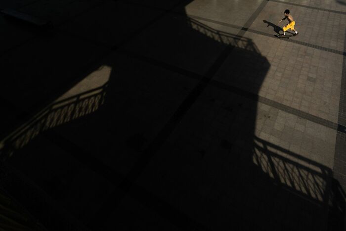 A person in yellow pants running on a paved street with strong shadows in pure street photography style.