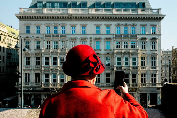 Person in a red hat and coat taking a photo in an urban setting, showcasing pure street photography awards style.