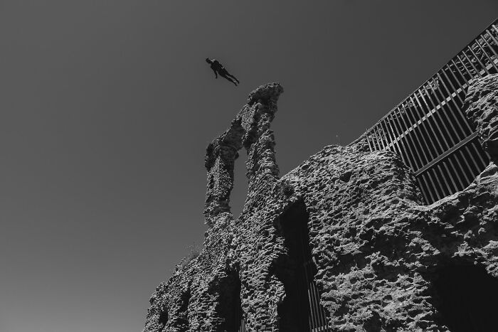 Black and white image showing an urban scene with a person jumping near ruins, capturing pure street photography energy.