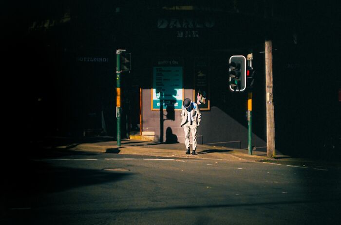 Man in light suit and hat standing alone on an empty street corner capturing the essence of street photography.
