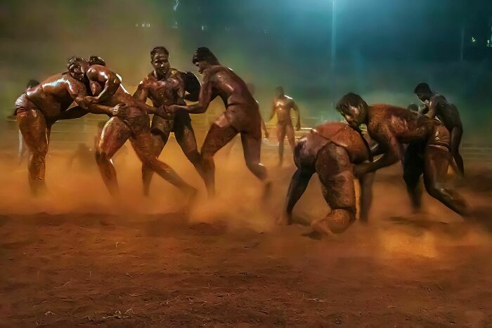 Men wrestling on a dusty street at night, captured in a dynamic moment showcasing raw street photography energy.