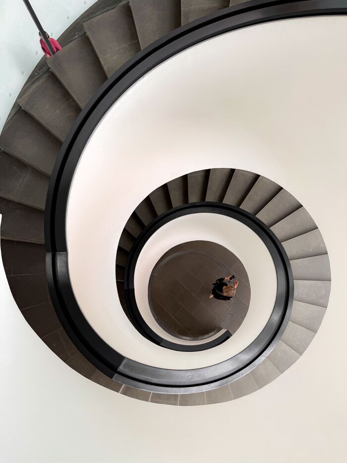 Spiral staircase viewed from above with a person at the bottom, capturing a pure street photography moment.
