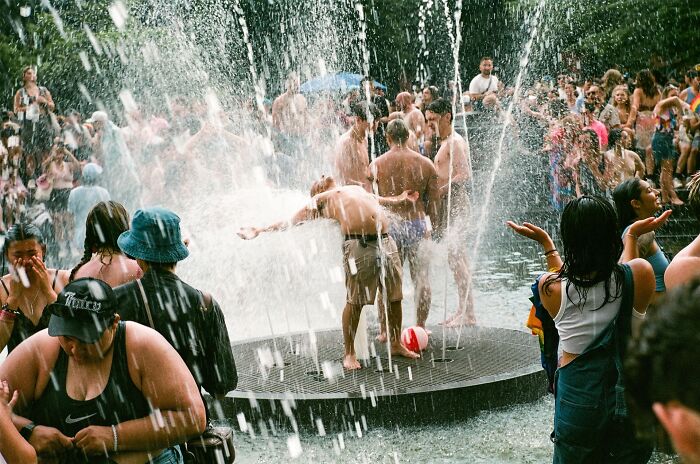 Crowded urban fountain scene with diverse people enjoying water on a warm day in vibrant street photography style.