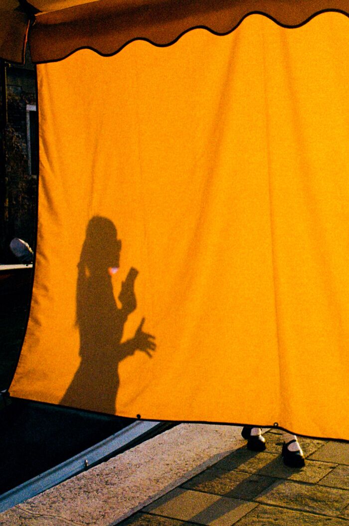 Shadow of a person holding a phone behind a yellow curtain, showcasing a candid moment in street photography awards.