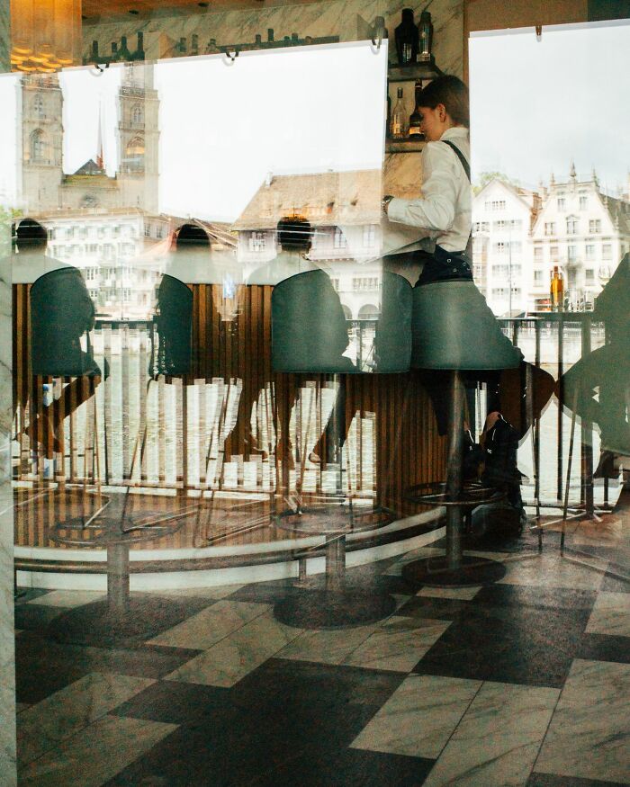 Reflection of people sitting and a waiter standing inside a cafe in a street photography awards winning image.