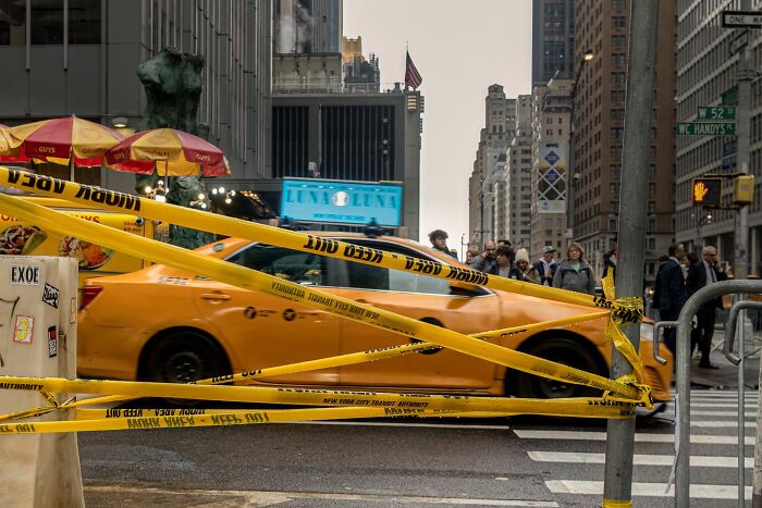 Yellow taxi passing through a busy city street with caution tape, capturing the essence of pure street photography awards.