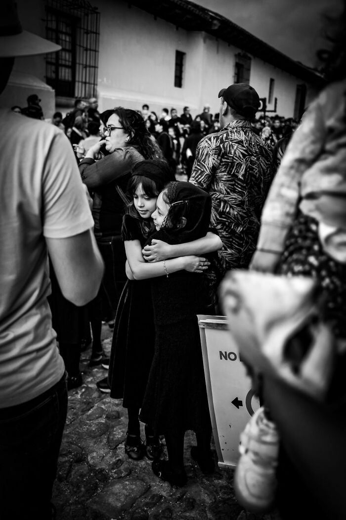 Two young girls hugging in a crowded street scene, captured with striking emotion in pure street photography.