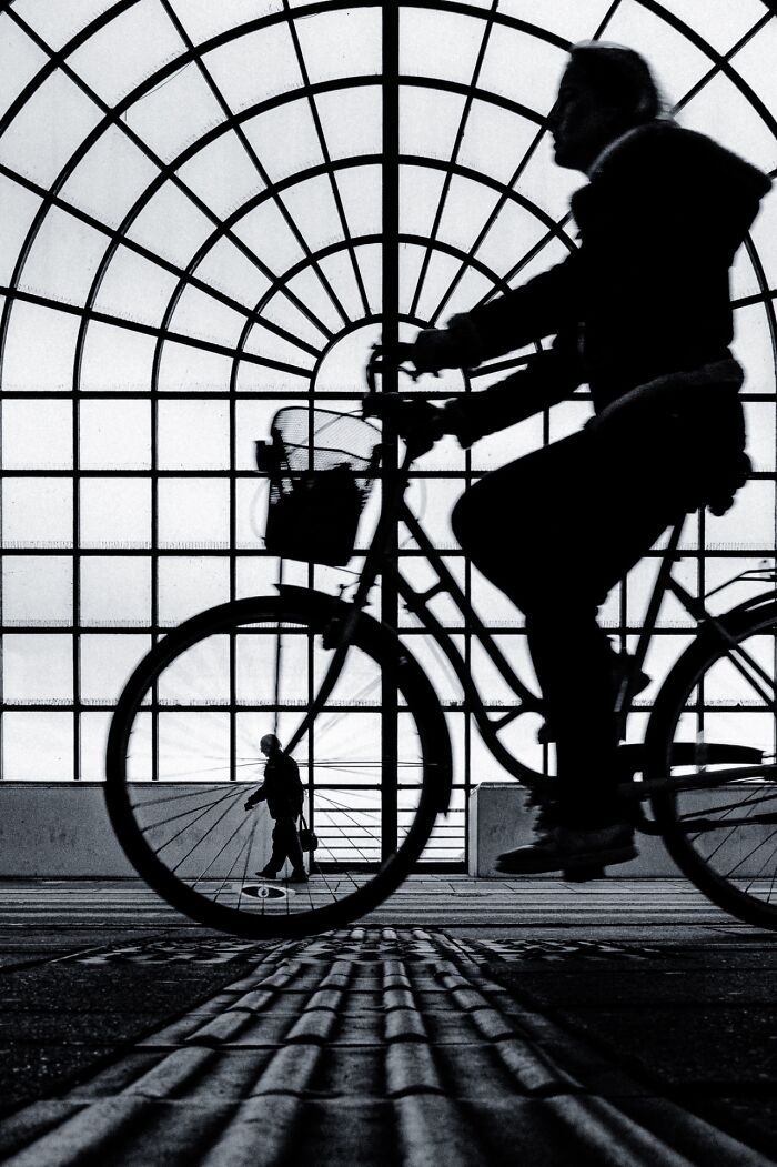 Silhouette of a cyclist in front of a geometric window, capturing pure street photography and the soul of the streets.