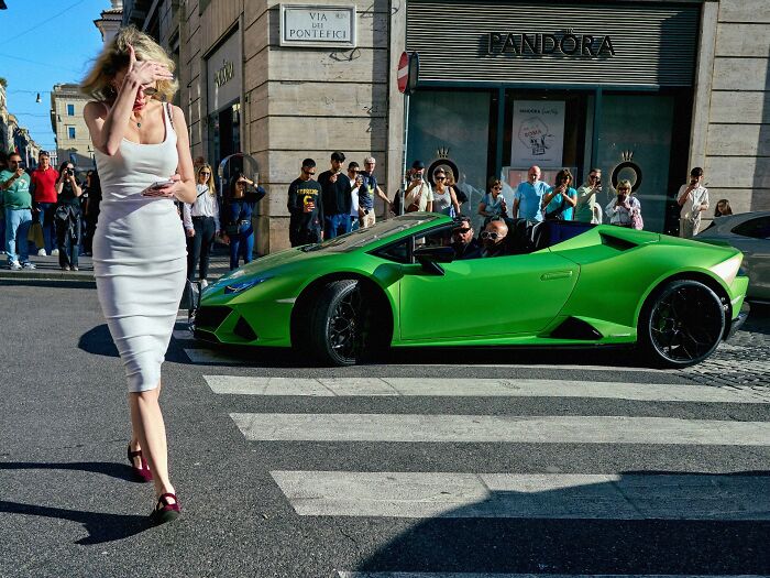 Woman in white dress crossing street, bright green sports car, and pedestrians capturing pure street photography moments.