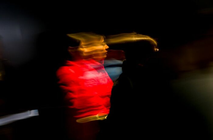 Abstract blurred image of a person in red jacket at night, showcasing motion and atmosphere in street photography awards.