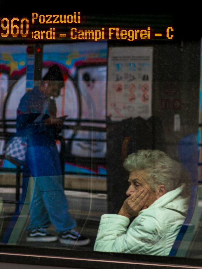 Elderly woman in a white coat sitting on a bus, reflecting urban life in a pure street photography award-winning image.