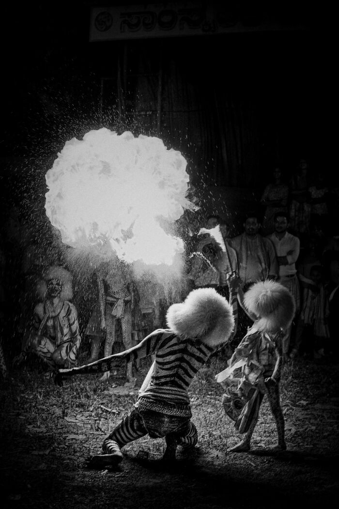 Black and white street photography image of performers with fire breath and traditional costumes capturing raw street moments.