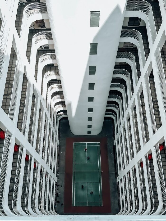 Aerial view of an urban courtyard with a tennis court surrounded by tall white buildings, capturing pure street photography.