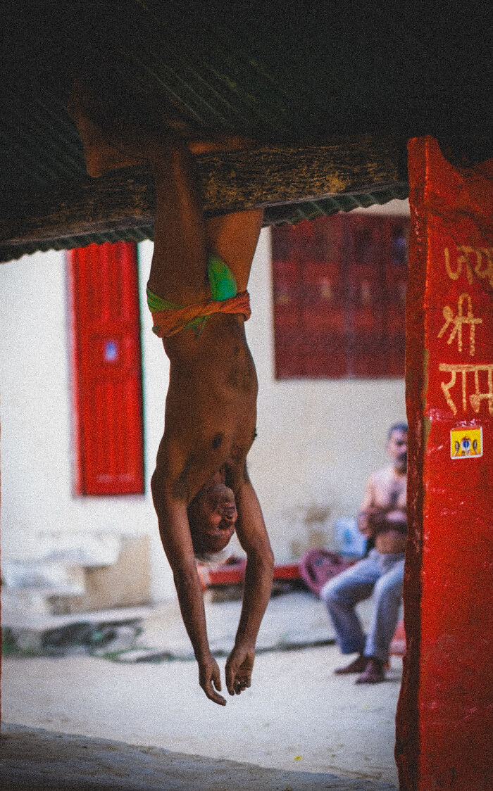 Man hanging upside down from a roof beam in an urban setting, captured in pure street photography awards style.