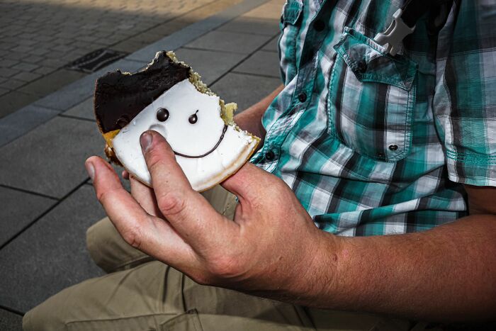 Close-up of a person holding a half-eaten smiling face cookie captured in street photography style outdoors