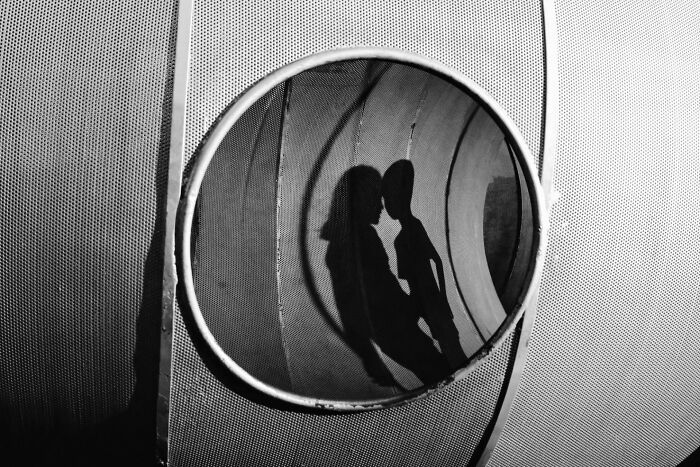 Shadow of two people kissing reflected in a round mirror, capturing an intimate moment in street photography.