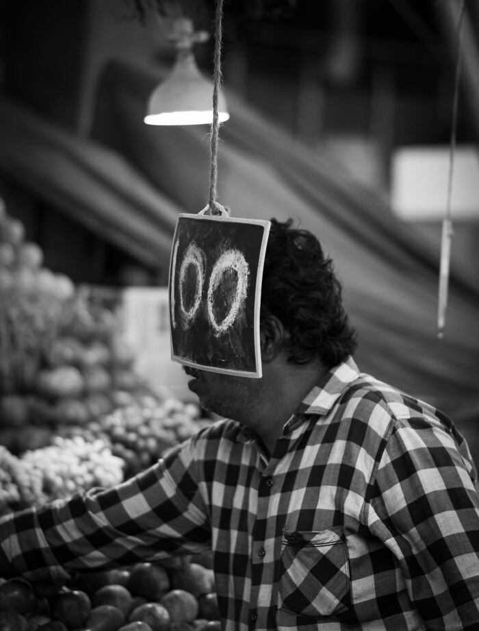 Black and white street photography of a man at a market, with a price sign hanging in front of his face, Pure Street Photography Awards.