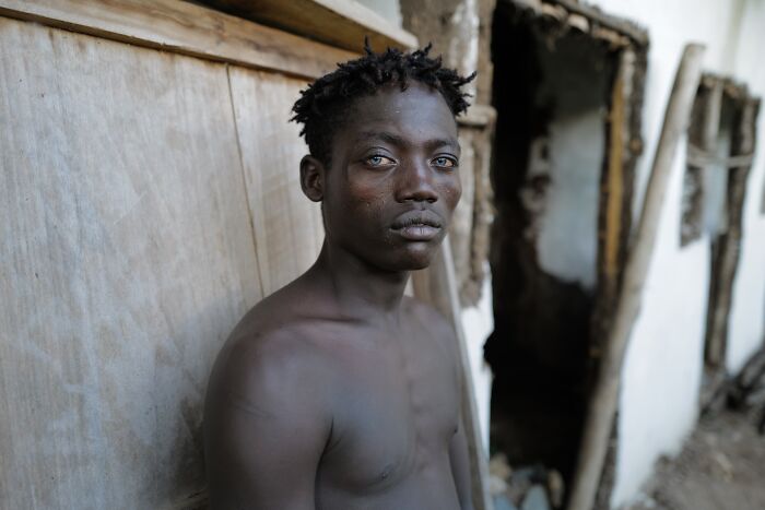Young man with intense gaze leaning against weathered wall in urban setting, capturing raw emotion in street photography.