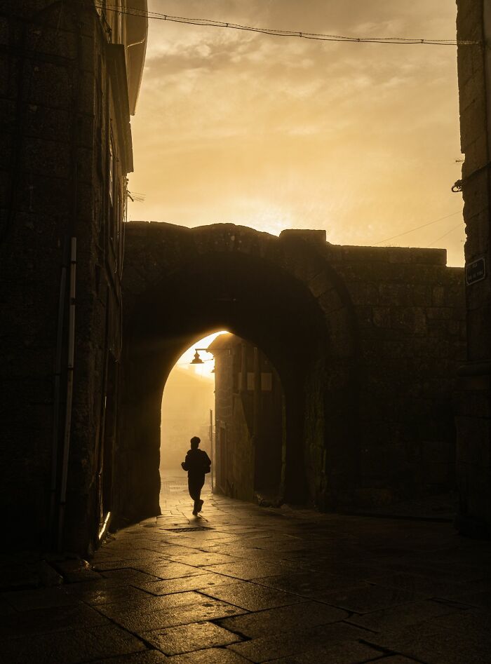 Silhouette of a person walking through an old stone archway at sunset captured in street photography awards.