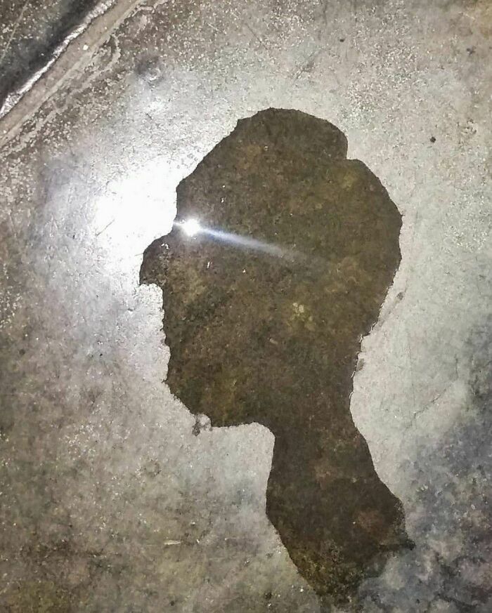 Shadow of a person reflected in a puddle on the street, capturing a raw moment of pure street photography.