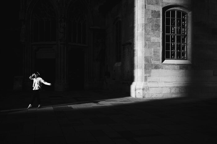 Woman walking in dramatic light and shadow on a city street, captured for Pure Street Photography Awards 2025.