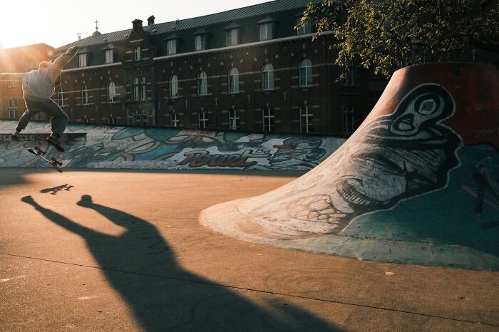 Skateboarder performing a trick in a graffiti-covered skatepark at sunset in a candid street photography scene.
