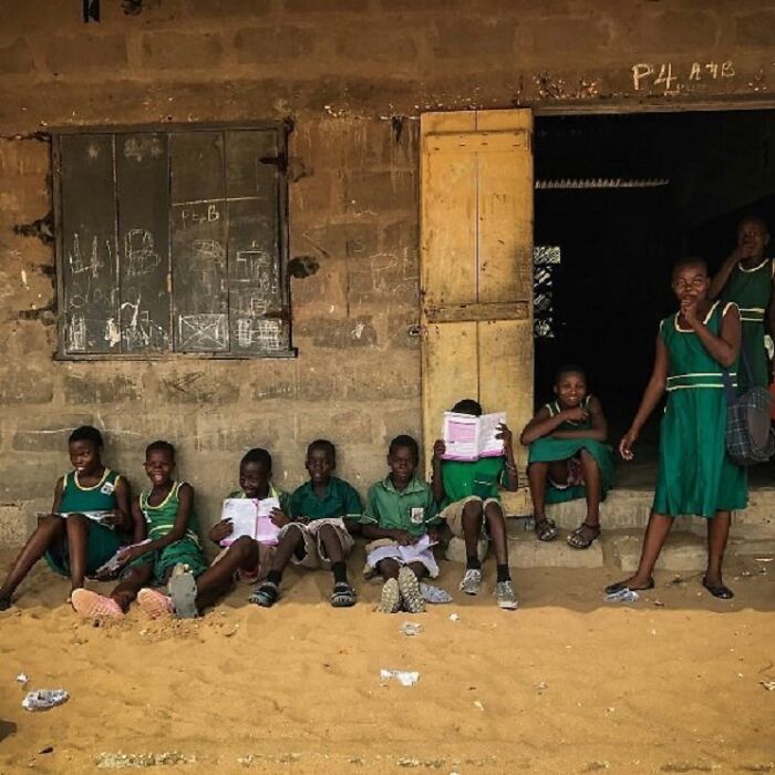 Children in green uniforms reading and sitting outside a rustic school building, showcasing childhood around the world.
