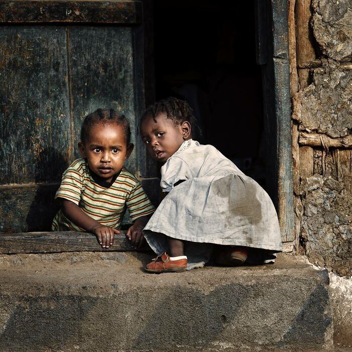 Two curious children at a doorstep in a rustic setting, capturing beautiful childhood moments around the world.