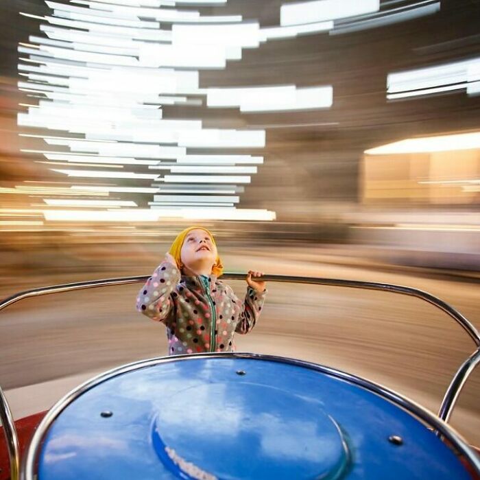 Child enjoying a spinning amusement ride, captured in a beautiful photo of childhood with motion blur and bright lights.