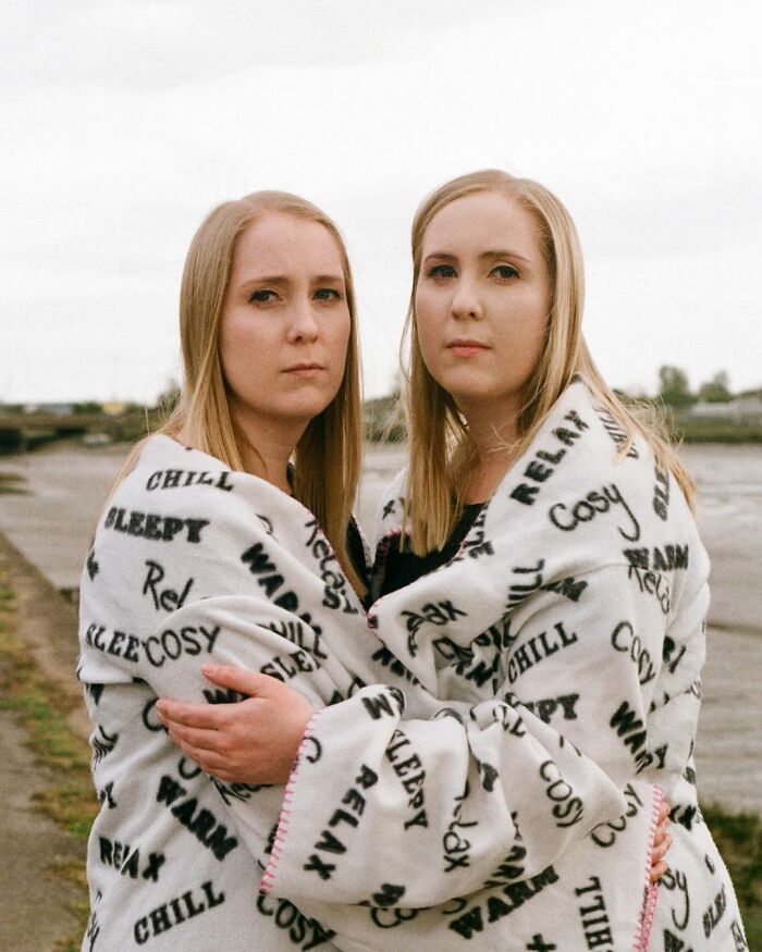 Twin sisters wrapped in a cozy blanket, showing their unique bond in a natural outdoor portrait by a London photographer.