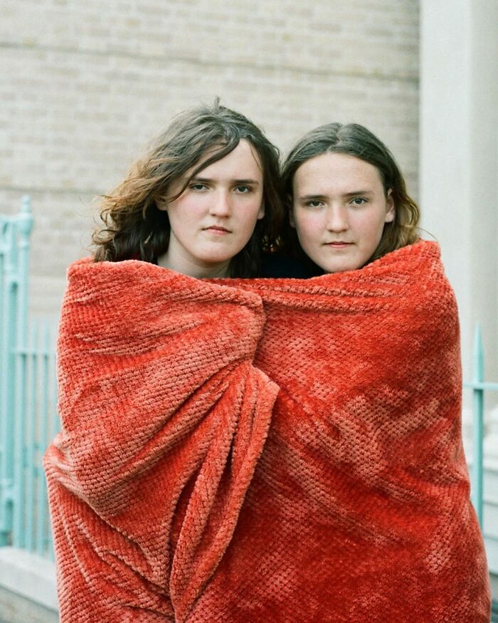Two twins wrapped together in a red blanket, captured by a London photographer showcasing their unique bond.