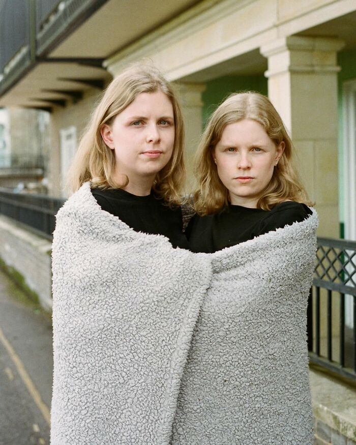 Twin sisters wrapped in a blanket in an outdoor setting, London photographer captures their unique bond in portraits.