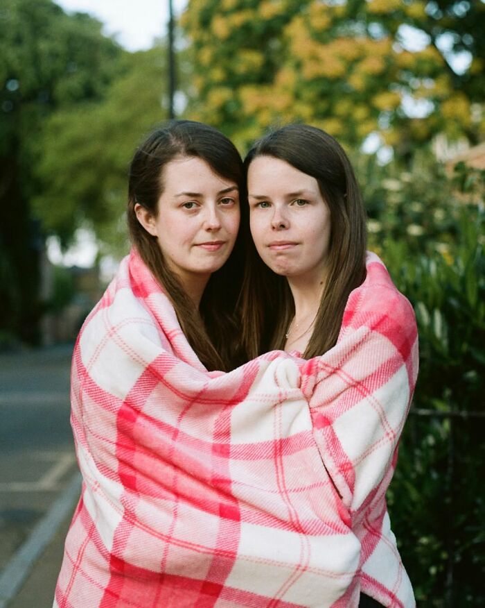 Two twins wrapped in a pink plaid blanket outdoors, captured by a London photographer showcasing their unique bond.