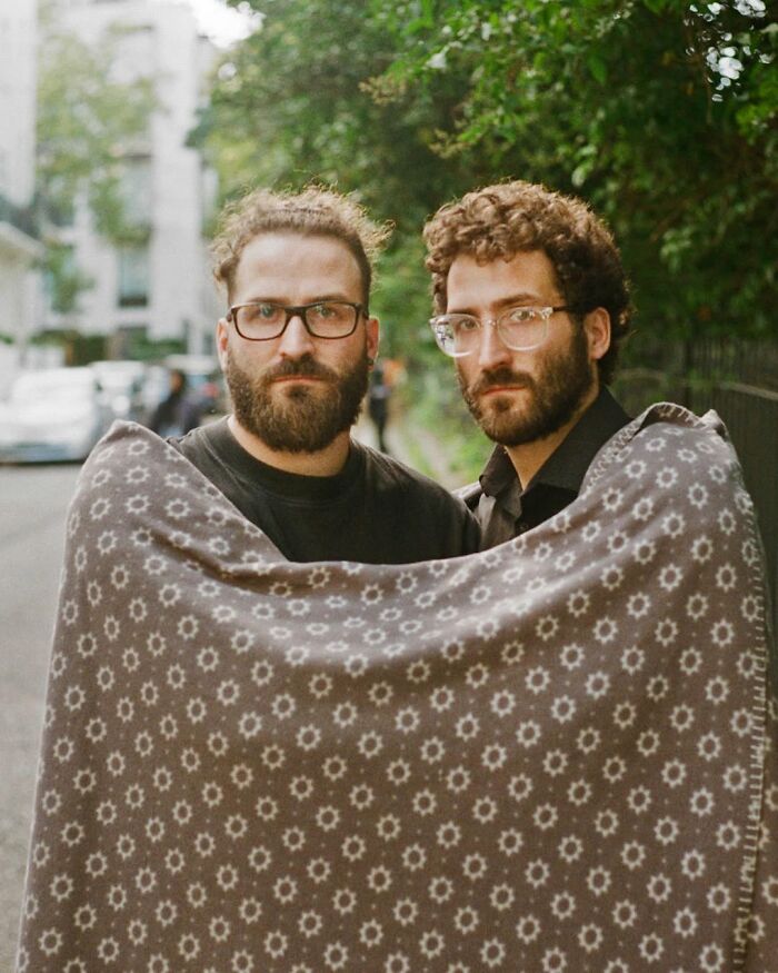 Two bearded men wearing glasses share a patterned blanket in a portrait by a London photographer capturing twins' unique bond.