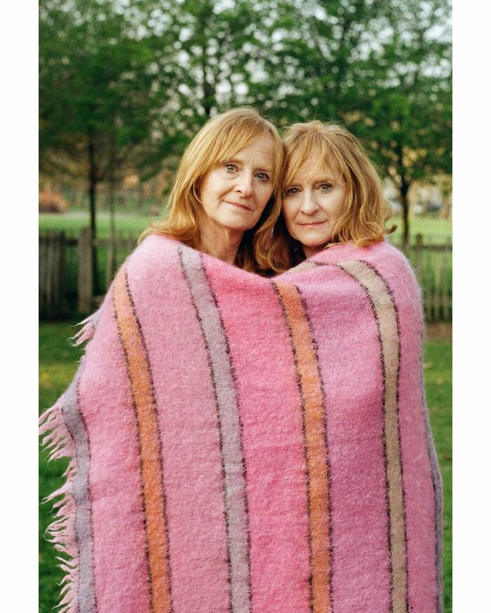 Twin sisters wrapped in a pink striped blanket outdoors, captured by a London photographer in a stunning portrait.