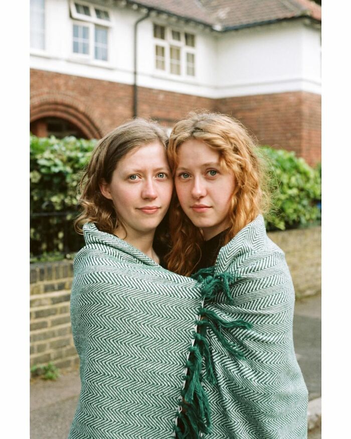 Two young women wrapped in a blanket, captured by a London photographer showcasing the unique bond between twins.