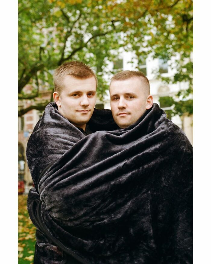Two twin brothers wrapped together in a black blanket outdoors, captured by a London photographer in a stunning portrait.