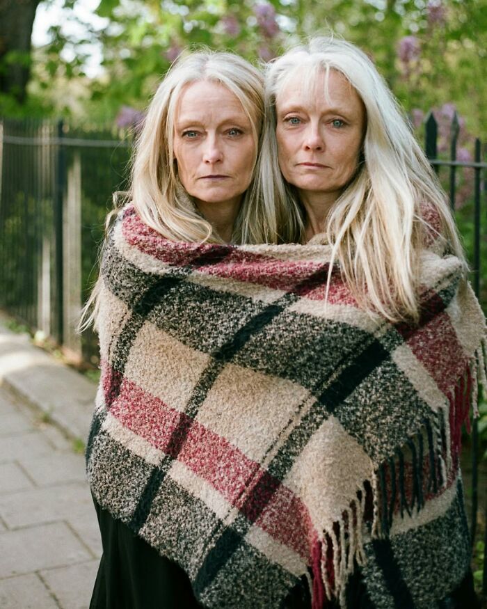 Twin sisters wrapped in a checkered blanket, captured by a London photographer showcasing their unique bond outdoors.