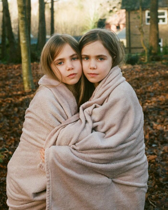 Twin girls wrapped in beige blankets outdoors, captured by London photographer showing their unique bond in a stunning portrait.