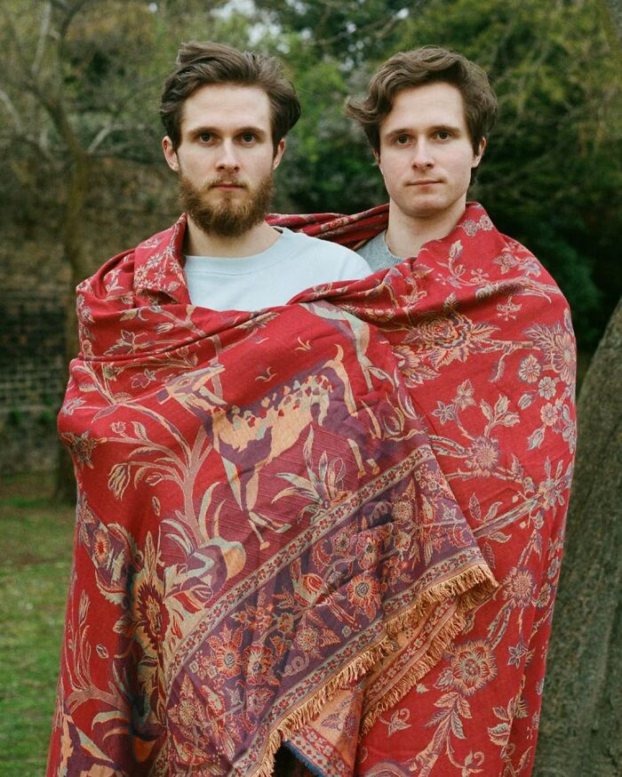Two young men wrapped together in a red patterned cloth outdoors, captured by a London photographer focusing on twins.