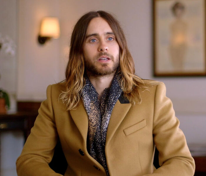 Man with long hair and beard wearing a brown coat and patterned scarf, illustrating disappointment in someone idolized.