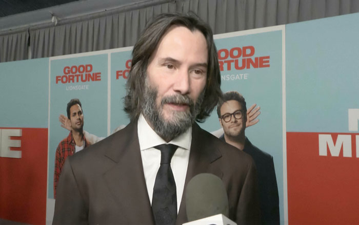 Keanu Reeves in a brown suit speaking to media, addressing Alexandra Grant marriage rumors at a movie premiere event.
