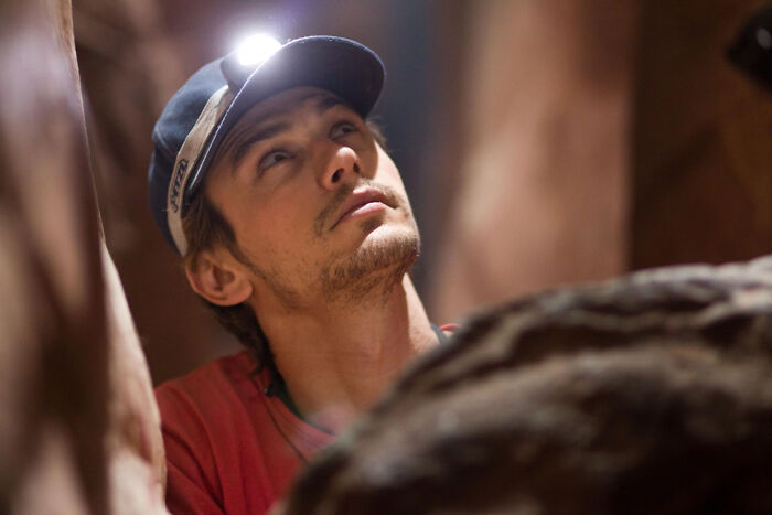 Man wearing a headlamp in a narrow rocky space, scene from movies based on true stories that feel impossible to believe