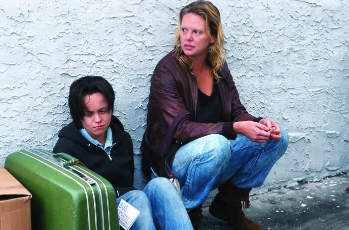 Two women sitting on the ground with a green suitcase, depicting a scene from movies based on true stories.