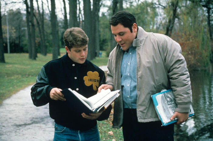 Two young men outdoors reviewing a large book, a scene from movies based on true stories that feel impossible to believe.