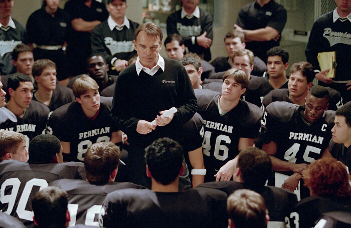 Coach delivering an intense team talk to football players in a locker room scene from movies based on true stories.