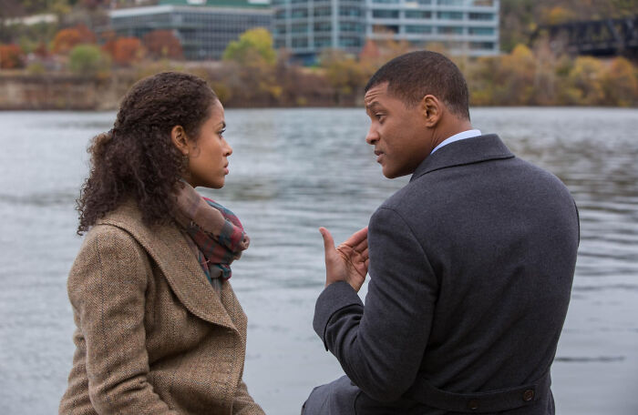 Two people having a serious conversation by a riverbank in a scene from movies based on true stories.