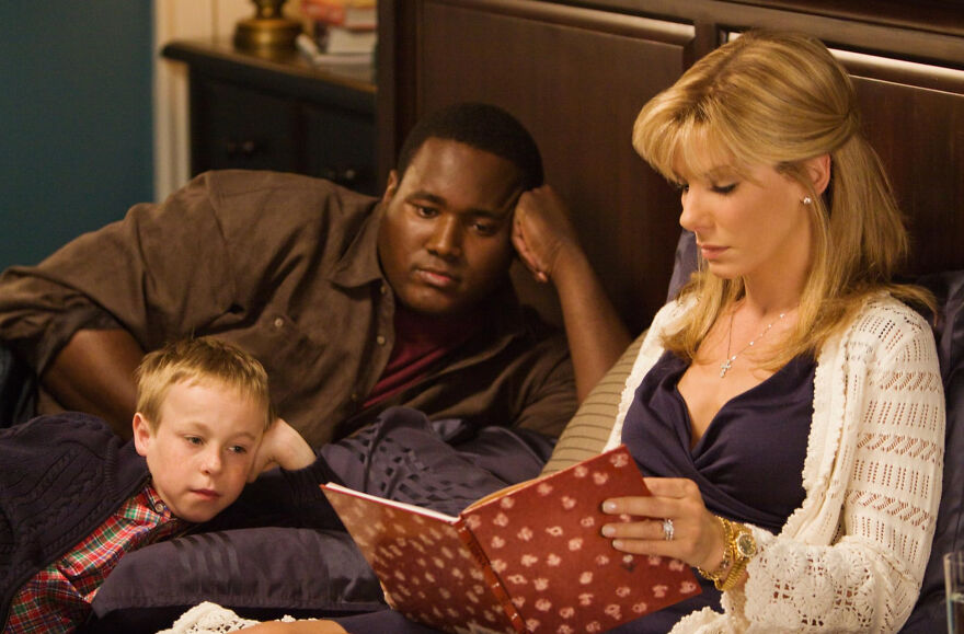 A woman reads a book to a man and child on a bed, depicting a scene from movies based on true stories.