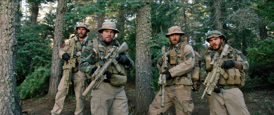 Four soldiers in tactical gear holding rifles, standing alert in a dense forest scene from a movie based on true stories.